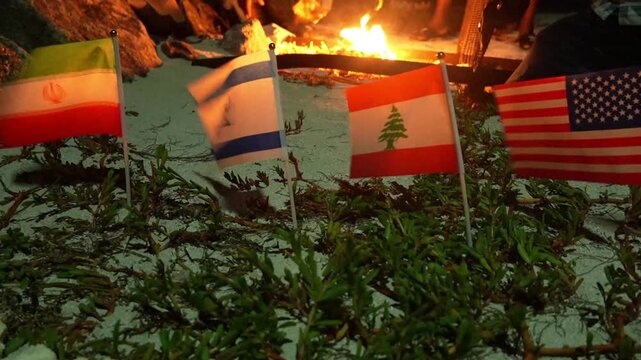 Israeli, Lebanese, and American flags are positioned near a bright fire at night.