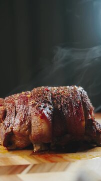 Video of a whole boneless roasted pork joint resting on a wooden board with visible steam rising. The crispy, seasoned crust and rich texture emphasize freshly cooked, hearty comfort food and slow roa
