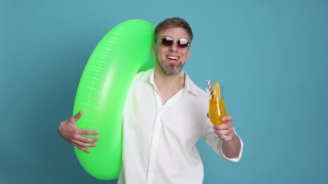 Handsome man with cocktail and inflatable ring on light blue background