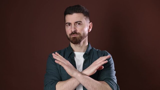 Man shaking head and crossing arms expressing disagreement on brown background