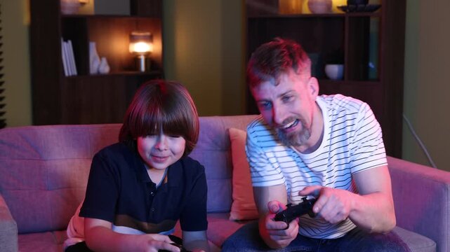 Emotional father and son with controllers playing video game on sofa at home