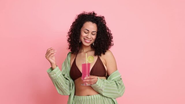 Beautiful woman in beachwear with cocktail on pink background