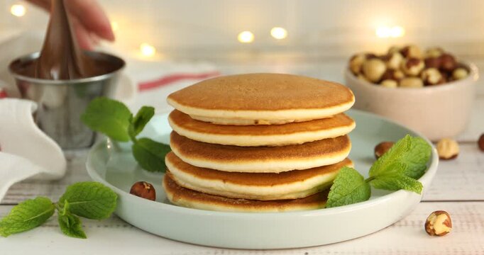 Woman spreading chocolate paste onto pancake at light wooden table, closeup