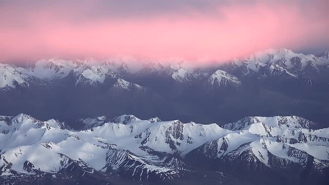 Aerial Andes scene shows ice covered summits, pink cloud layer, golden sunset rays. Airplane window frames Andean cordillera, snowcapped ridges under rose haze during twilight flight.