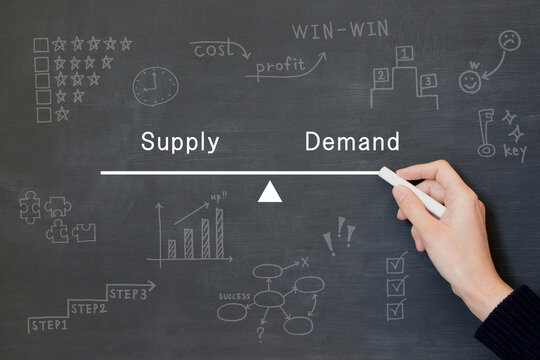 需要と供給のバランスをイメージしたシーソーを黒板に描く人物の手