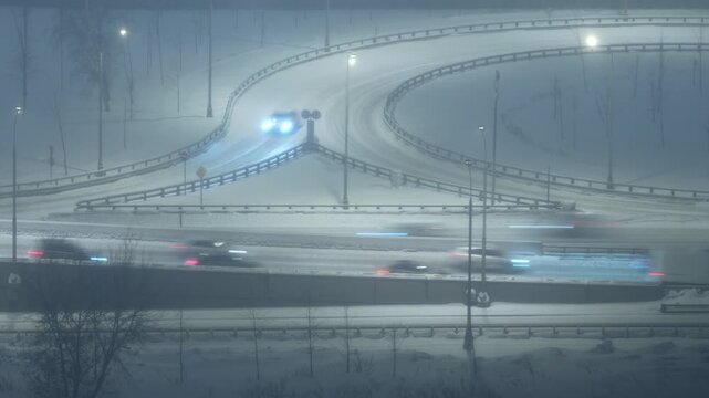 Night highway interchange in snowfall, cars moving on snowy roads, winter traffic, low visibility urban transport scene