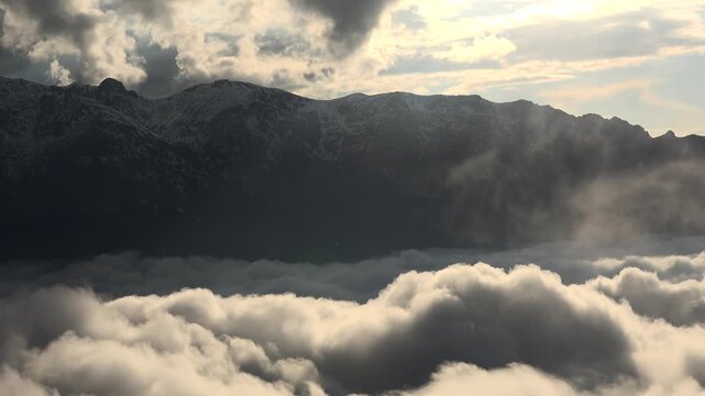 Alps mountain peaks rise above cloud sea as sunrays pierce mist, cinematic landscape view. Swiss range summits overlook overcast layer, god rays through vapor, breathtaking highland vista.