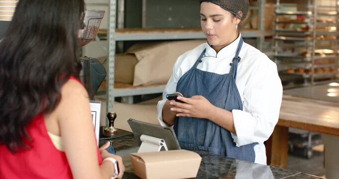 Female customer and staff in chef coat lifting phone, checking POS and confirming order at bakery