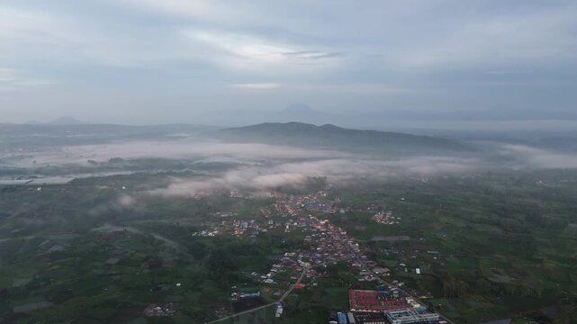 Aerial drone view from a bald hill in Karo Highlands, North Sumatra, Indonesia, showing layers of Bukit Barisan mountains covered with beautiful white clouds in the fresh morning light.