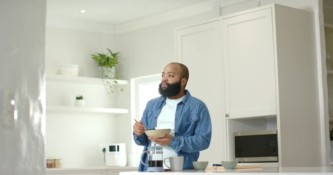 African American man at island holding bowl, spoon stirring to prepare breakfast near French press