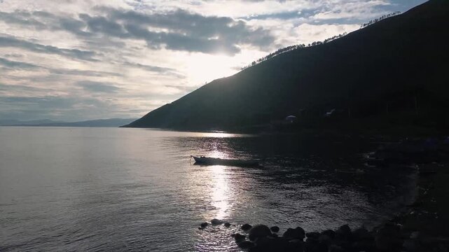 Cinematic drone shot slowly moving to the left, capturing the soft silhouette of morning light over Lake Toba in Silalahi, North Sumatra, Indonesia. A small traditional fishing boat gently drifts on t