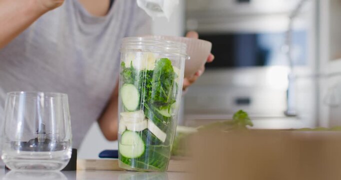 African-American woman approaching kitchen counter spooning yogurt into blender cup making drink