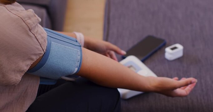 African American woman sitting on sofa, cuff on left arm, pressing monitor, watching BP readings