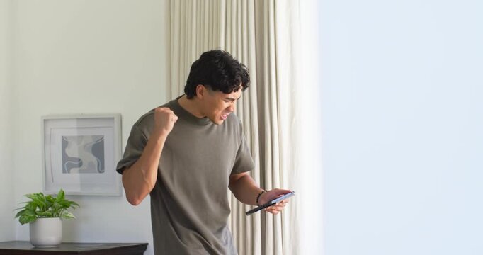 Man standing near glass door as curtain clears, tapping tablet, reacting to alert, pumping fist