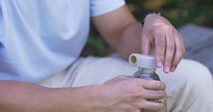 Adult man removing inner stopper and tilting reusable bottle, taking measured sips for health