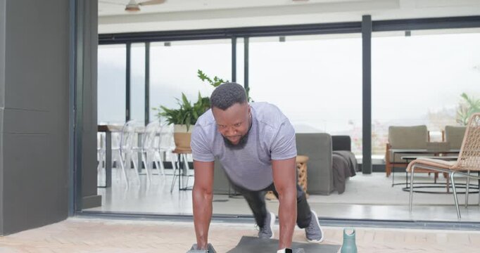 African American man in tee starting plank dumbbell-rows patio mat resting and drinking to hydrate