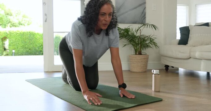African descent woman starting plank, doing knee drives in sneakers on green mat at home, cuing