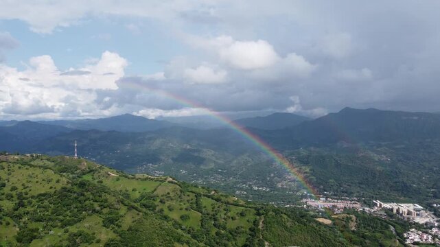 aerial shot, drones flying over a beautiful green mountains near a rainbow and villeta city in the Cundimarca region in Colombia. Cloudy day 4K