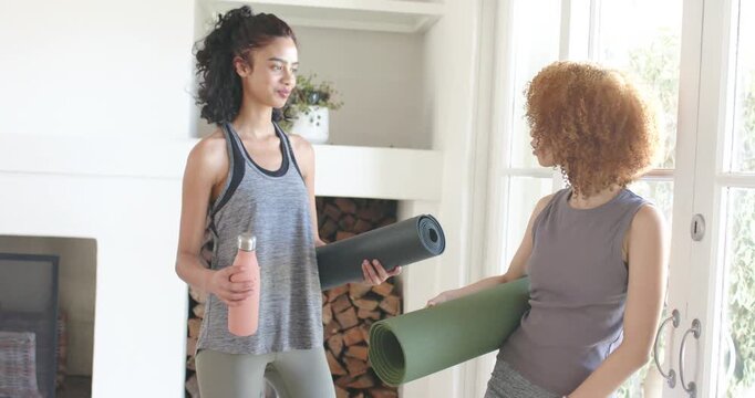 African American women chatting as right woman gesturing holding yoga mats starting workout at home