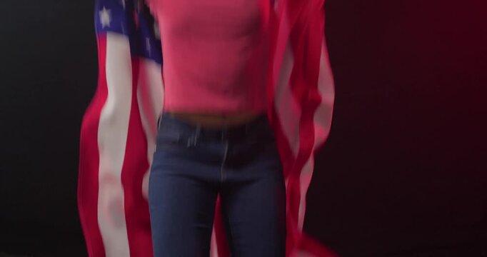 Waving woman wearing pink tee and jeans lifting American flag from turf to overhead in studio