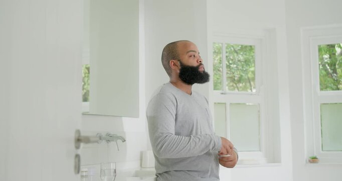 African American man checking wrists, opening pill bottle with red cap, taking medication at sink