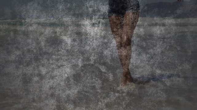 Woman walking through shallow surf at beach, denim shorts splashing water around ankles