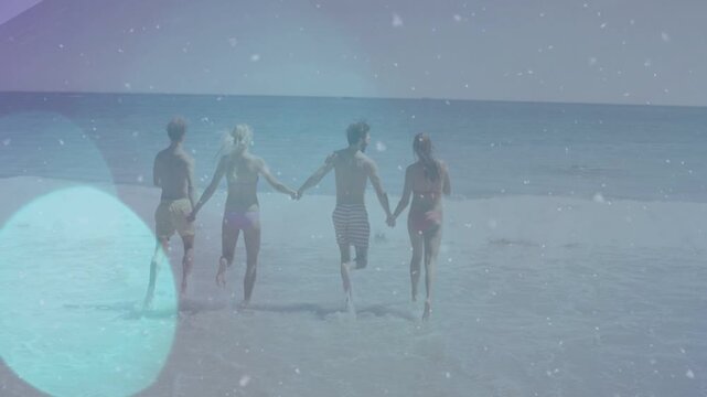 Four adults holding hands breaking into run from sudden impulse, wading toward ocean with bokeh