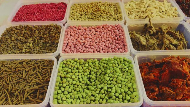 Tracking shot of assorted Indian mukhwas and digestive snacks in clear plastic containers, showing colorful goli, crispy sev, and spiced mixtures arranged neatly in a vibrant mela market setting!