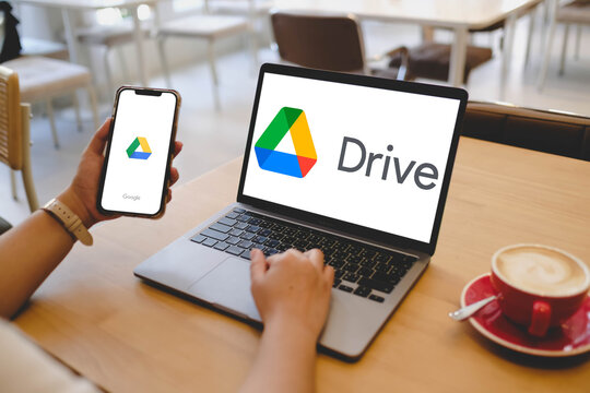 Bangkok, Thailand. April 15, 2026; A person is using a MacBook Pro laptop and a smartphone that both display the Google Drive cloud storage logo while sitting at a cafe table.