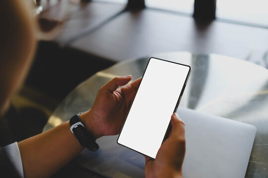 An over the shoulder view of a person holding a smartphone featuring a blank white mockup screen for custom content placement.