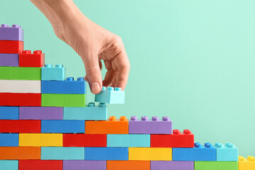 Female hand with colorful plastic building blocks on turquoise background