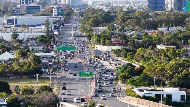 Aerial view capturing the dynamic flow of traffic on a busy multilane road through a city, with cars moving in both directions, framed by suburban landscapes and distant urban skyline.