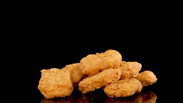 Close up hand picking up golden crispy chicken nugget from pile on black background with reflection.