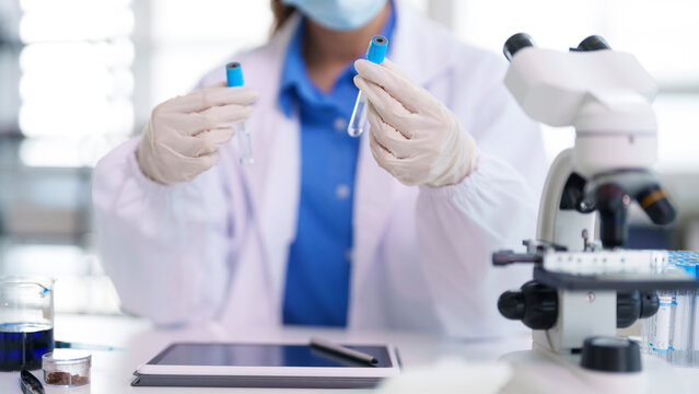 Asian adult scientist researcher conducting medical analysis lab experiment holding test tubes wearing mask gloves white coat modern laboratory environment