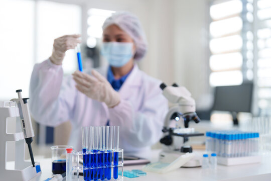 Asian adult woman scientist researcher conducting experiment examining test tube blue liquid for scientific research medical development in modern sterile lab