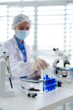Adult Asian scientist experiment blue liquid test tubes laboratory medical research scientific discovery pharmaceutical biotechnology innovation