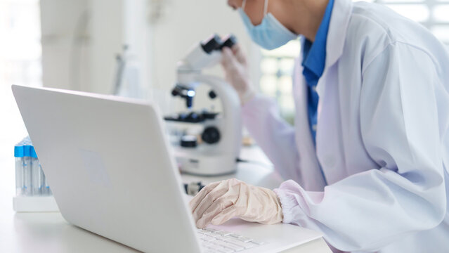Asian adult scientist researcher medical professional performs scientific research experiment analyzes data records findings using technology in modern laboratory