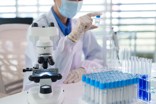 Asian adult scientist researcher holds vaccine vial sample prepares experiment in modern biology lab facility medical science pharmaceutical investigation development