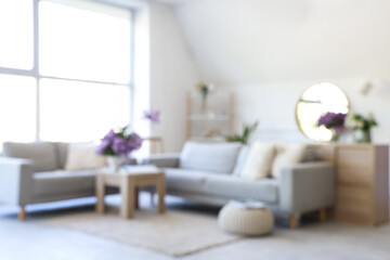 Naklejka premium Blurred view of light living room with sofas and lilac flowers in vases