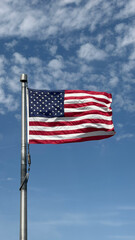 Obraz premium American flag waving in the wind with some clouds in the blue sky.