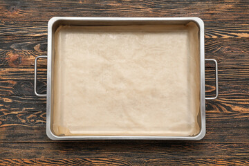 Naklejka premium Metal baking tray with parchment paper on wooden background
