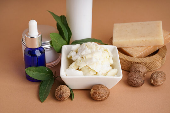 Bowl of shea butter, nuts and cosmetic products on color background