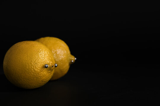 Fresh lemons with nipple piercing on dark background