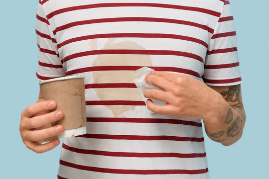 Young man with coffee stains on his striped t-shirt on blue background