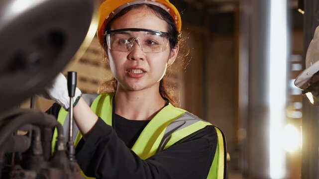 Female engineer in hard hat and safety glasses working on machinery with male colleague. Industrial professional team checking equipment in factory. Concept of technical maintenance and teamwork