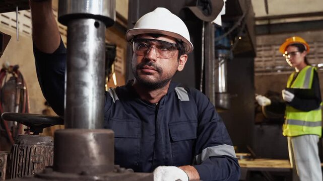 Professional male industrial engineer in a hard hat and safety glasses inspecting heavy machine with a wrench in a factory workshop. Maintenance technician repairing equipment in a plant manufacturing