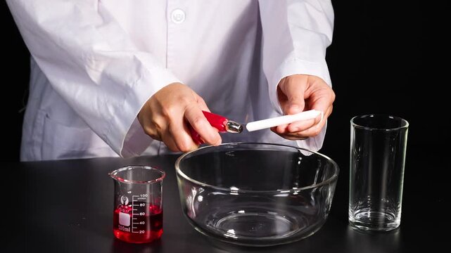 Scientist lighting white candle with red lighter inside empty glass bowl on dark laboratory desk.