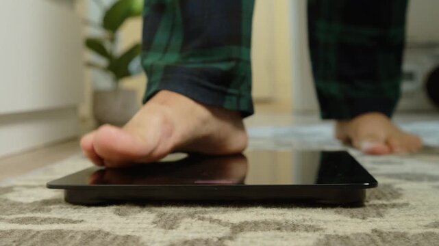 Macro close-up: male bare feet step onto a digital scale in a bright bathroom. Morning weight check, healthy lifestyle and self-care concept, realistic daily routine 4K.
