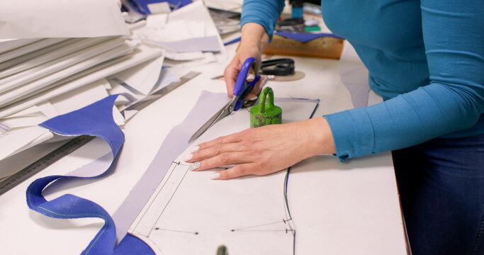 Apparel making. Tailor desk. Woman hand cutting fabric pressed with heavy weight. Making curved garment pattern with marks scissors.