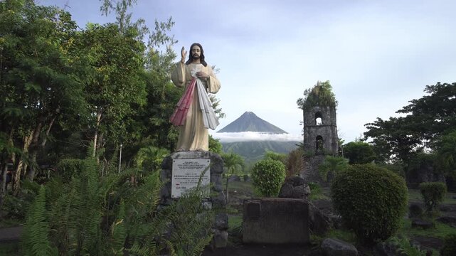 Statue of Jesus Christ in Cagsawa Ruins with iconic Mayon Volcano in background surrounded by tropical vegetation in Albay Philippines